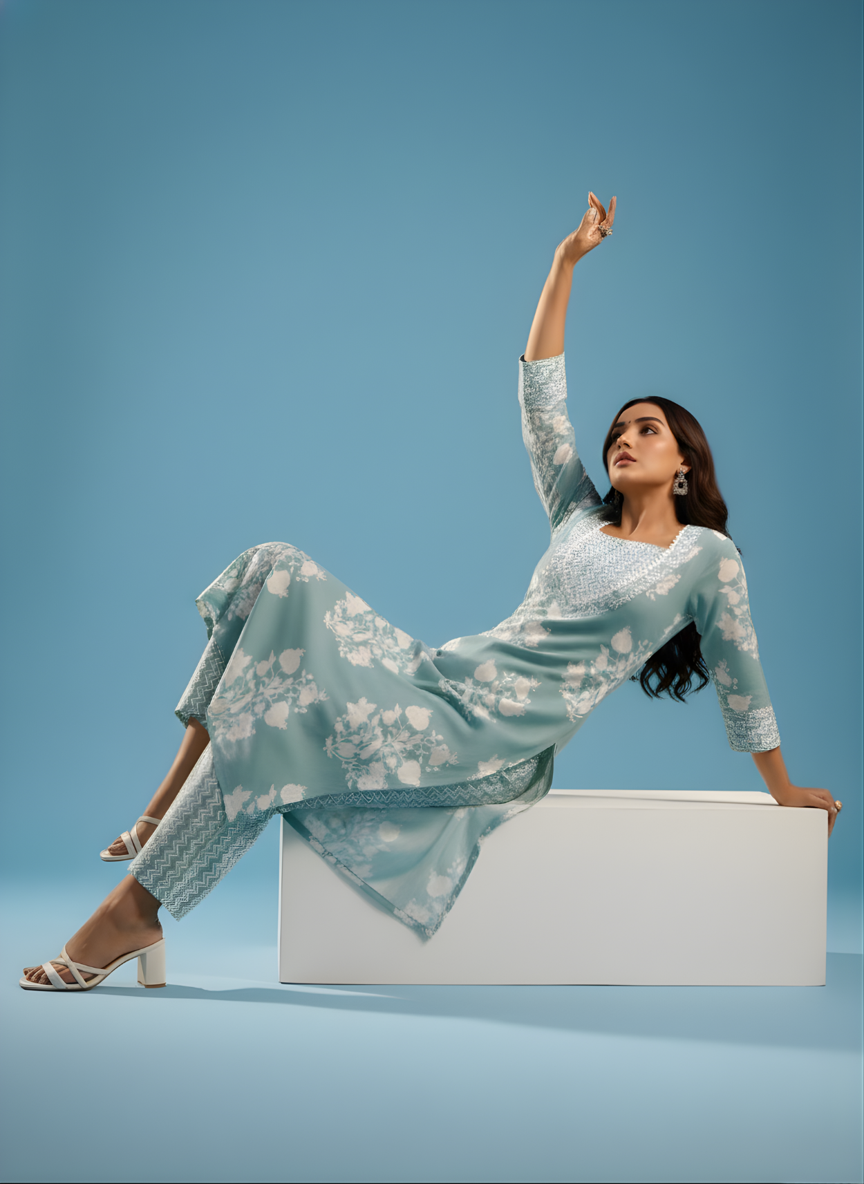Woman in a light blue floral dress sitting on a white box against a blue background