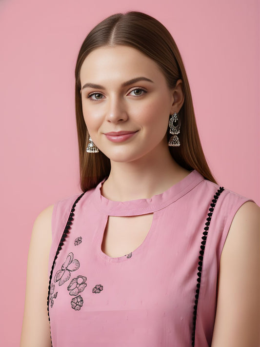 Woman wearing a pink top with black embroidery against a pink background