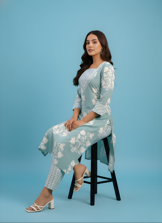 Woman in a light blue floral outfit sitting on a stool against a blue background