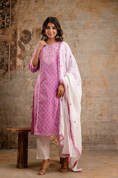 Woman wearing a pink and white traditional outfit with a patterned dress and white dupatta against a textured wall.