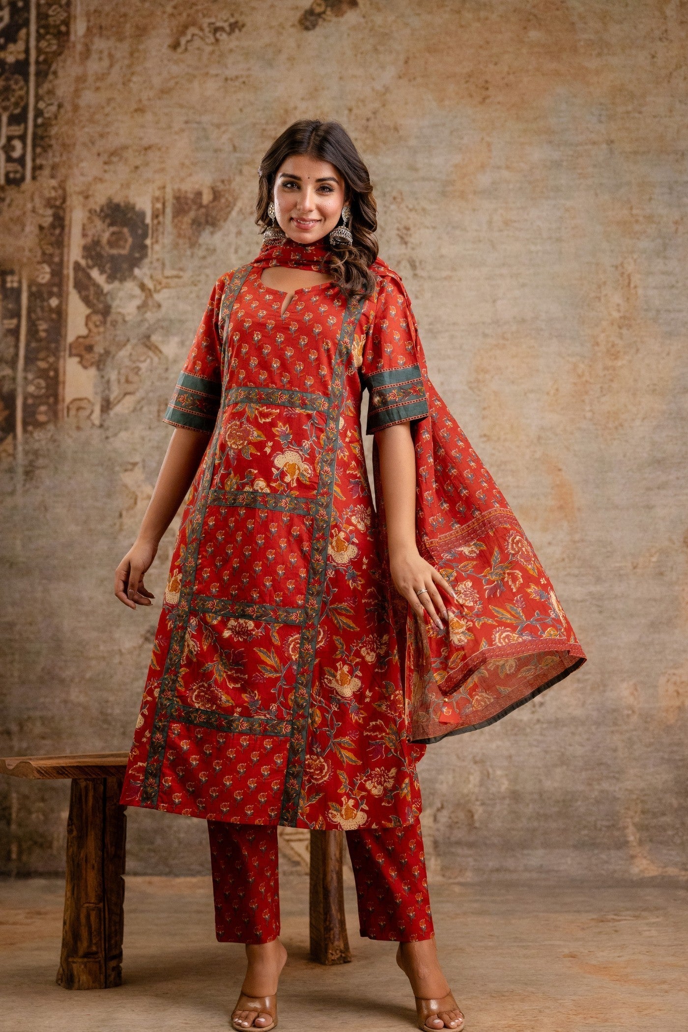 Woman wearing a red traditional outfit with floral patterns against a textured wall.