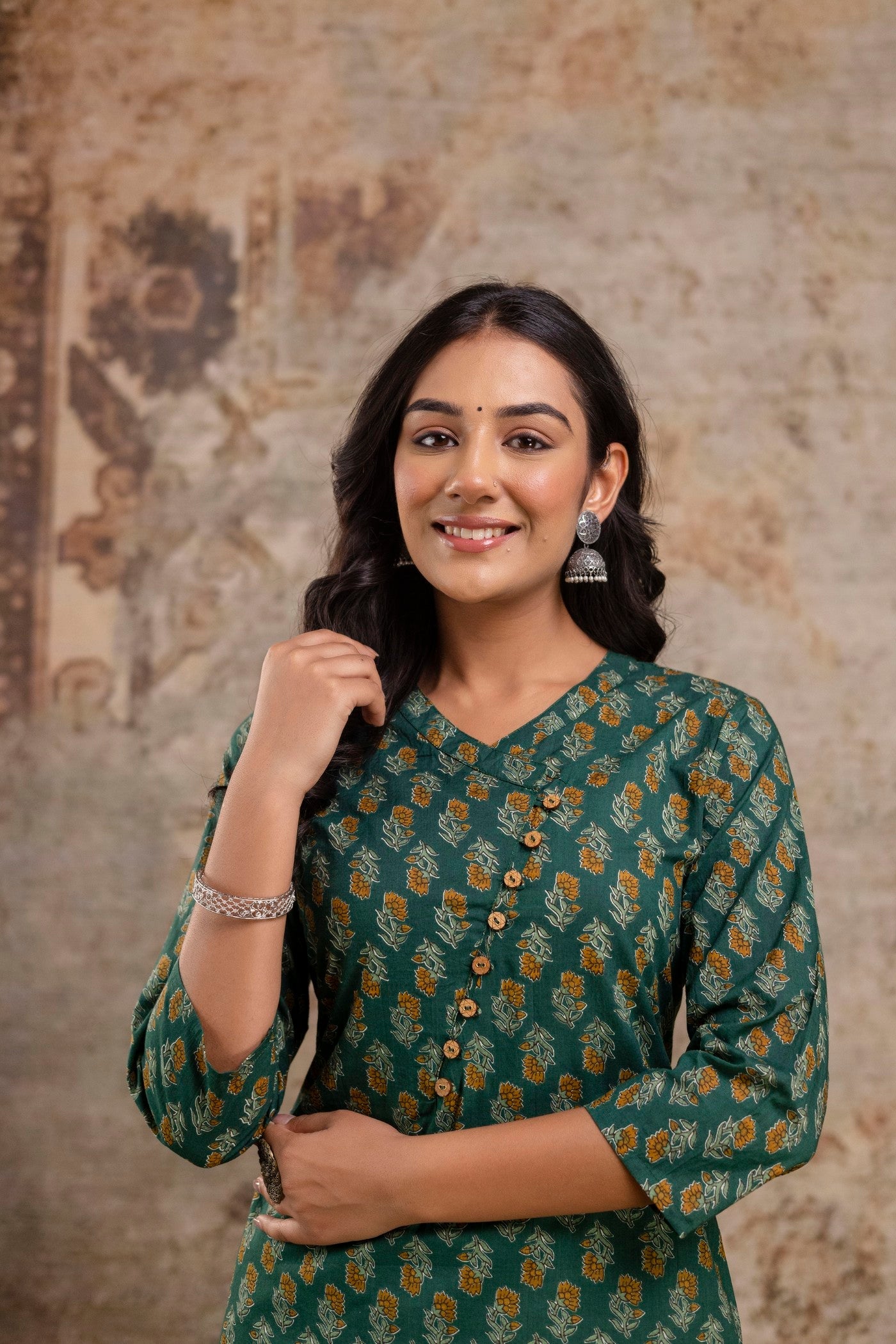 Woman wearing a green patterned dress against a textured wall.