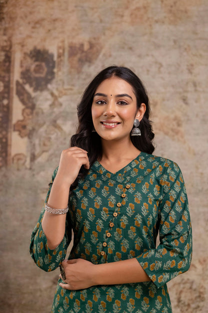 Woman wearing a green patterned dress against a textured wall.