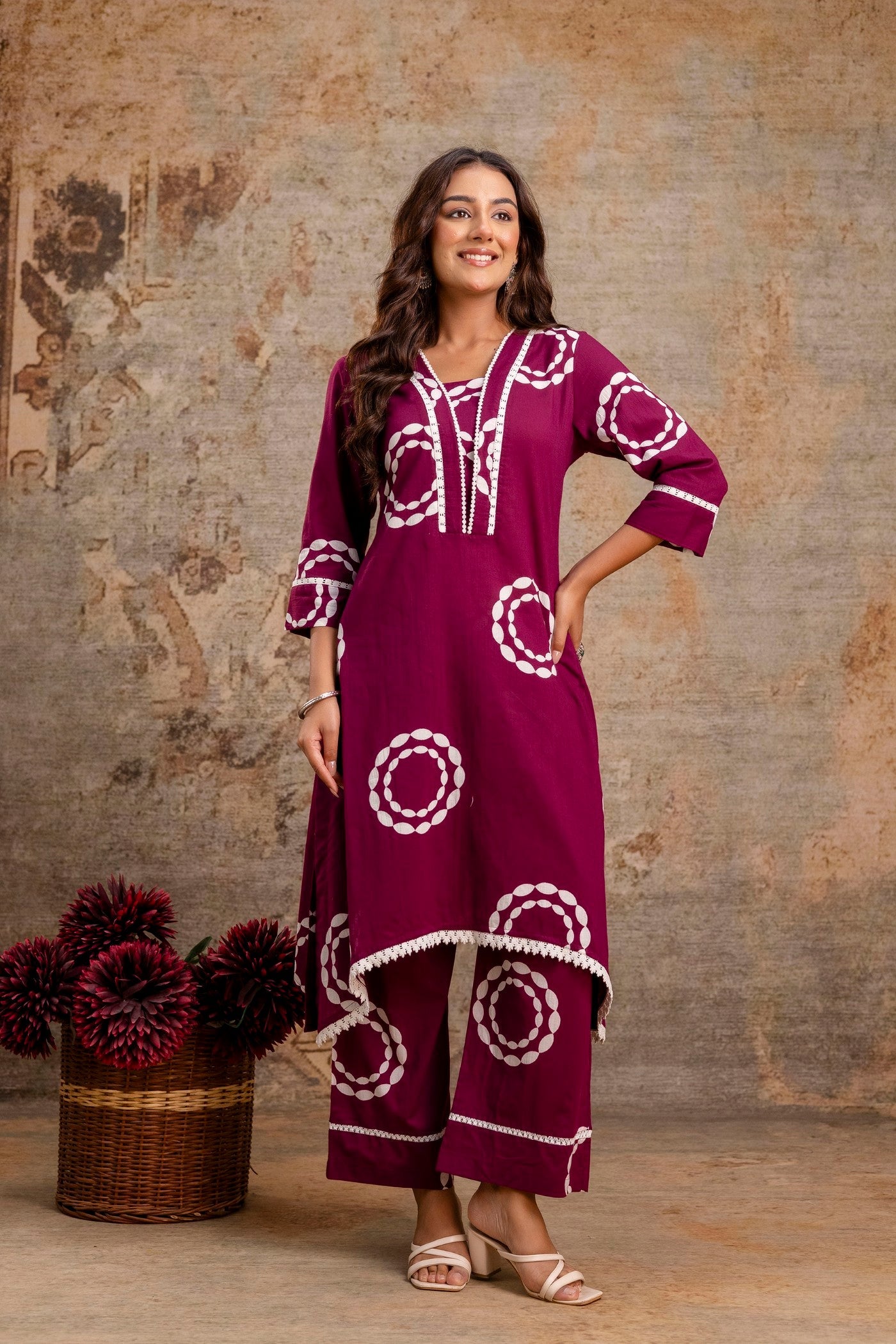 Woman wearing a purple outfit with white patterns against a textured wall.