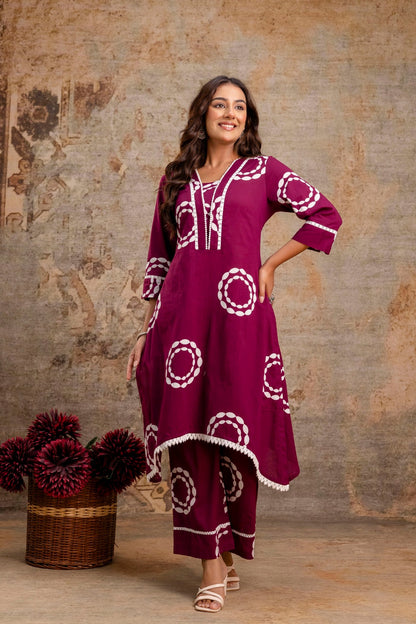 Woman wearing a burgundy dress with white patterns standing against a textured wall.
