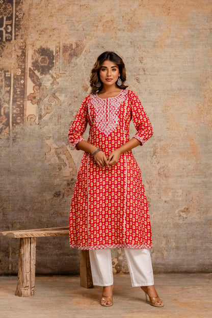 Woman wearing a red and white patterned kurta with white pants against a textured wall.