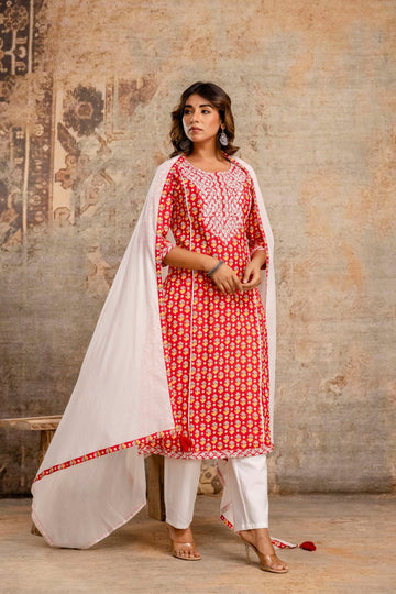 Woman wearing a red and white traditional outfit with a white dupatta against a textured wall.