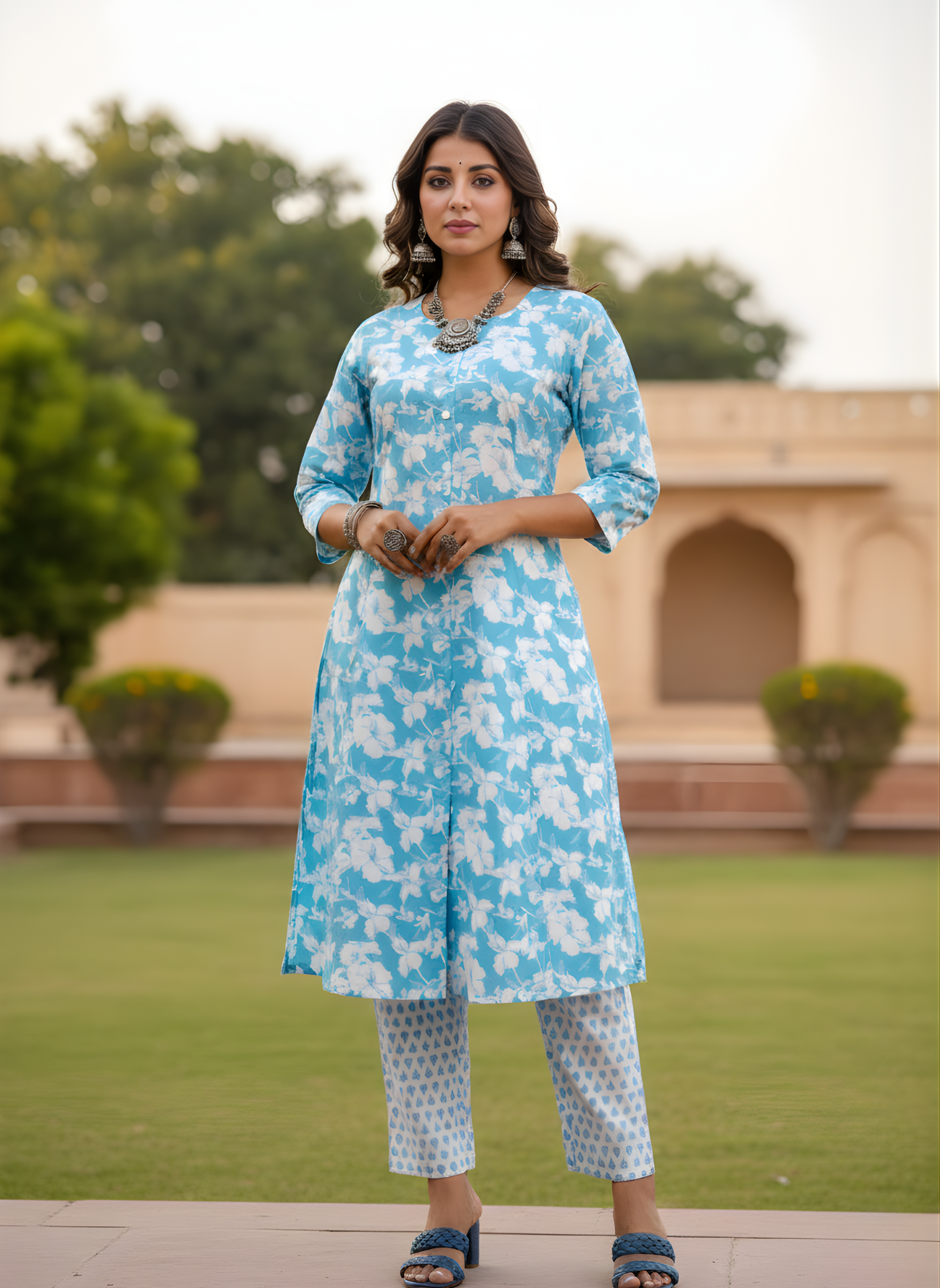 Woman wearing a blue floral kurta with white pants standing outdoors.