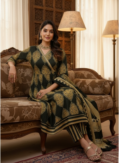 Woman in a green and gold traditional outfit sitting on a patterned sofa in a decorated room.