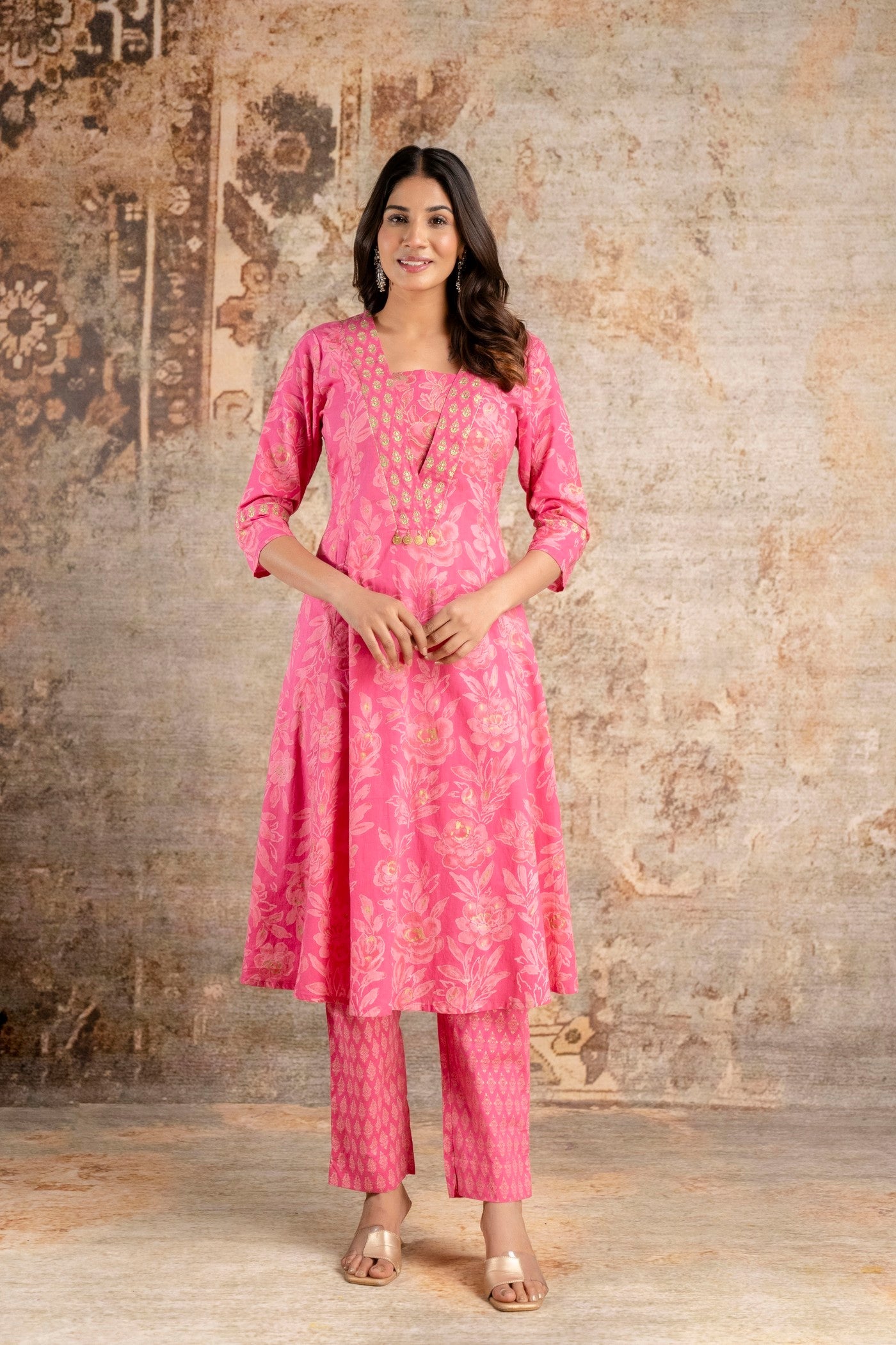 Woman wearing a pink traditional outfit against a textured wall.