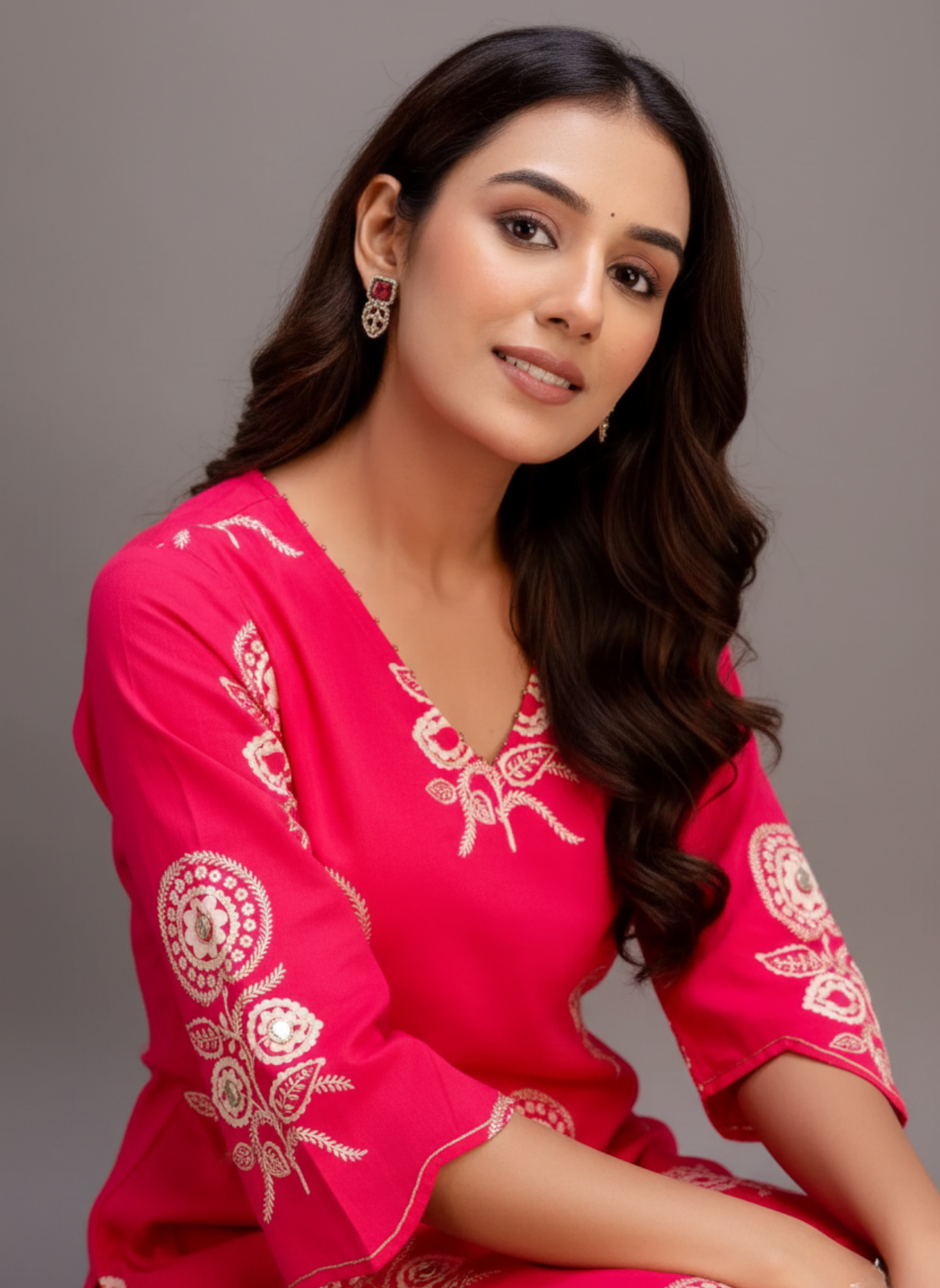 Woman wearing a pink traditional outfit with white embroidery on a gray background