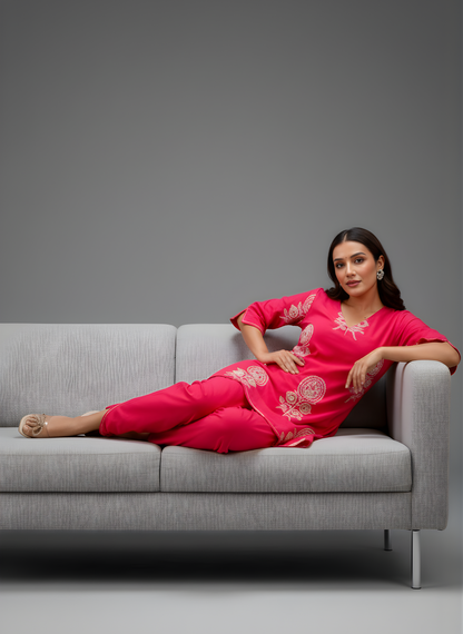 Woman in a pink traditional outfit sitting on a gray couch against a gray background