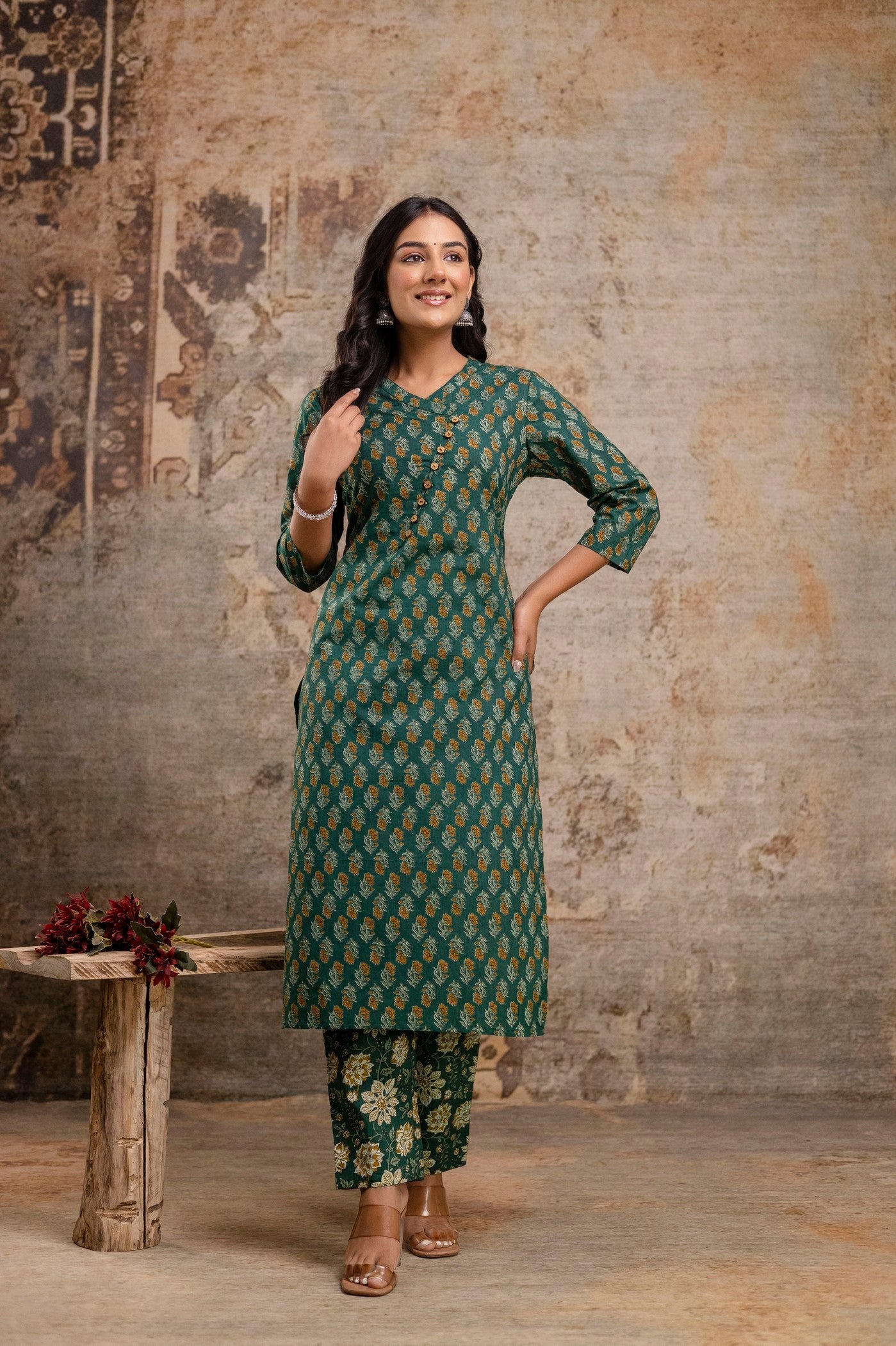 Woman wearing a green patterned outfit standing against a textured wall.