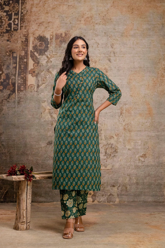 Woman wearing a green patterned outfit standing against a textured wall.